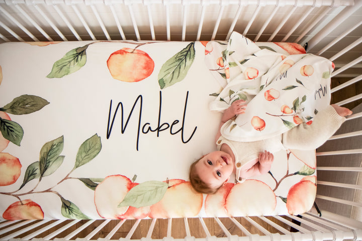 Baby on a custom crib sheet that has been personalized with her name and Georgia Peaches in watercolor art.