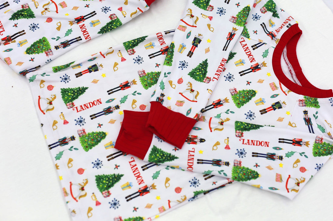 little boys wearing personalized Christmas pajamas featuring classic nutcracker images along with kid's name on white material and red cuffs.