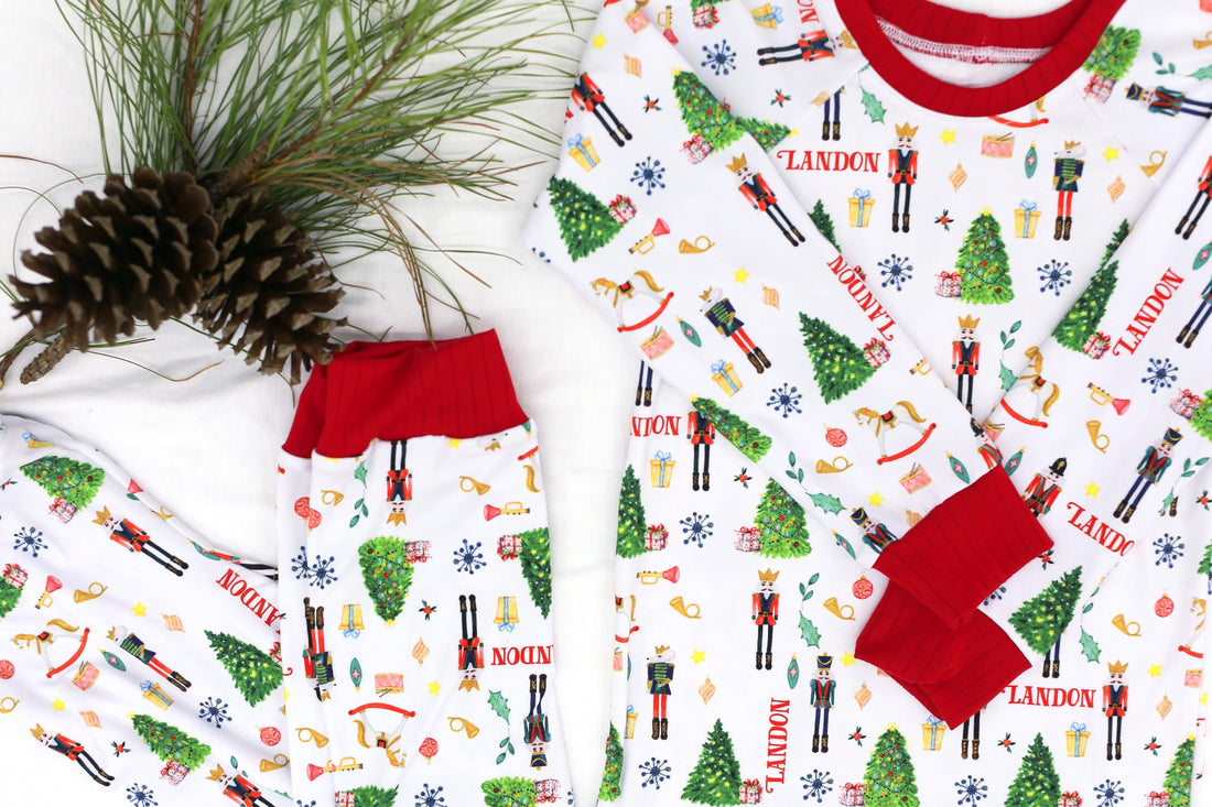 little boys wearing personalized Christmas pajamas featuring classic nutcracker images along with kid's name on white material and red cuffs.