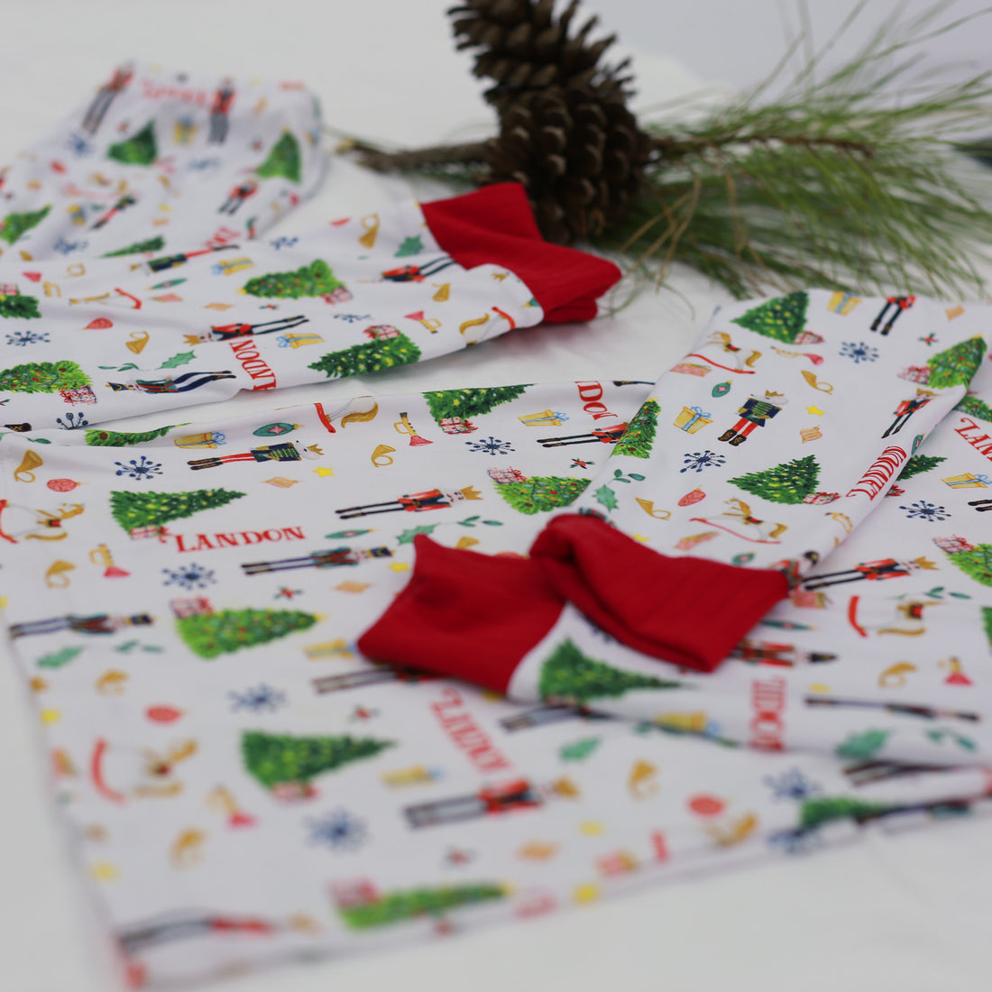 personalized Christmas pajamas featuring classic nutcracker images along with kid's name on white material and red cuffs.