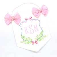 white and pink door hanging banner with baby's embroidered initials, two pink bows and a string for hanging on nursery or hospital door.