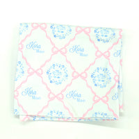 pink heirloom bow print personalized baby swaddle on white fabric and baby's name in light blue script font.