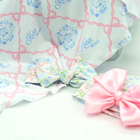 pink heirloom bow print personalized baby swaddle on white fabric and baby's name in light blue script font.
