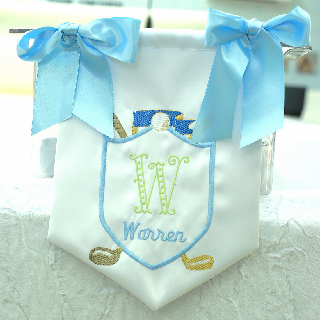 white satin door hanger for baby nursery or hospital room, blue bows on the corners, hanging string, embroidered initial and name with golf clubs and ball