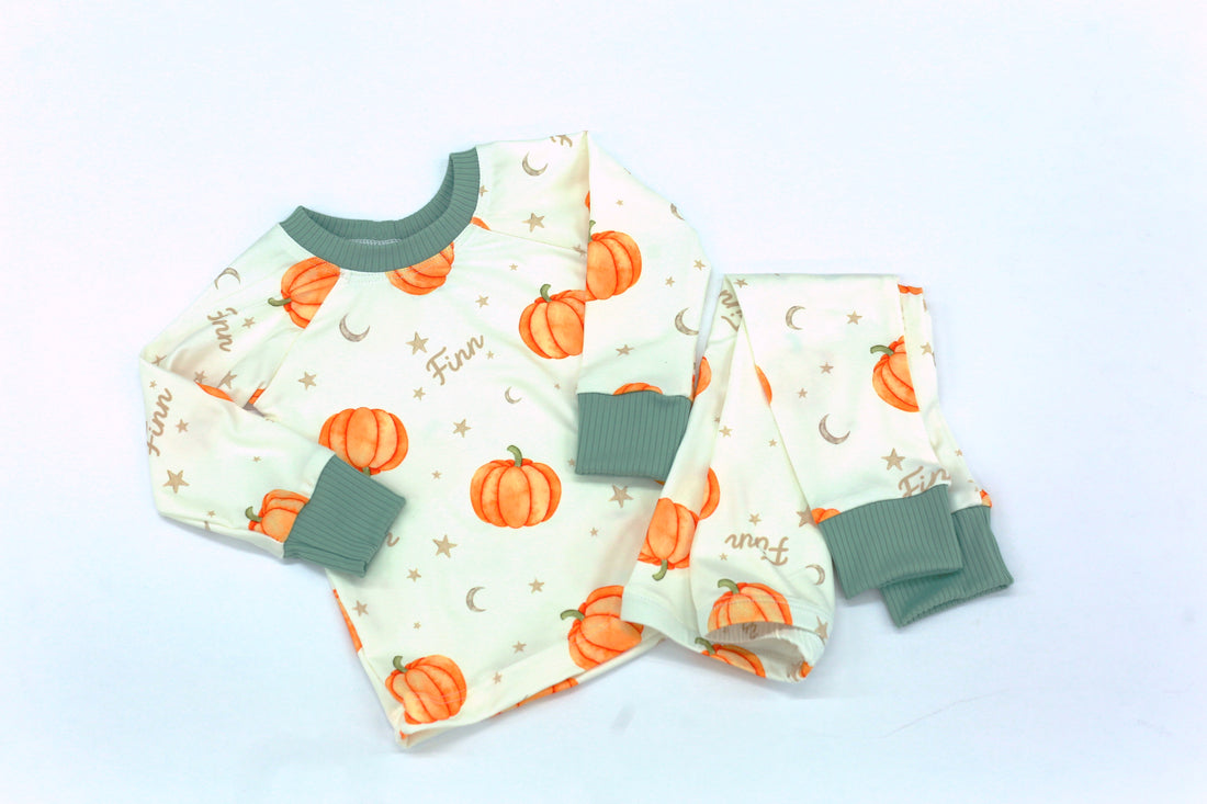 personalized Autumn PJs for little boys that have orange cartoon pumpkins and child's name in light brown letters on ivory fabric with green cuffs.
