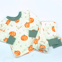 personalized Autumn PJs for little boys that have orange cartoon pumpkins and child's name in light brown letters on ivory fabric with green cuffs.