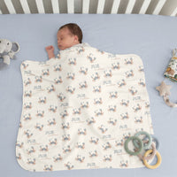 A sleeping baby wrapped in a blanket with a crab pattern, surrounded by toys on a light blue crib.