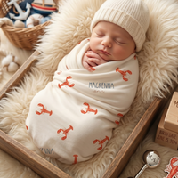 A newborn baby swaddled in a white blanket with red lobster patterns is peacefully sleeping in a wooden crate, surrounded by various baby items.
