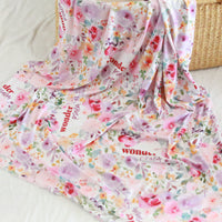 a colorful floral print blanket with the word "Wonder" printed on it. The blanket is spread out on a white surface, with a woven basket visible in the background.