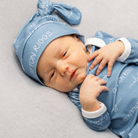 A newborn baby wearing a blue onesie with the name "CLAYTON RIGGS" printed on it, lying on a gray surface.