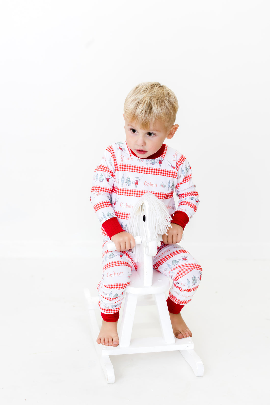 Little boy wearing personalized Modern Nutcracker Ballet for little boys with minimalistic images from the Nutcracker Ballet and his name with red checkered stripe pattern on white background and red cuffs.