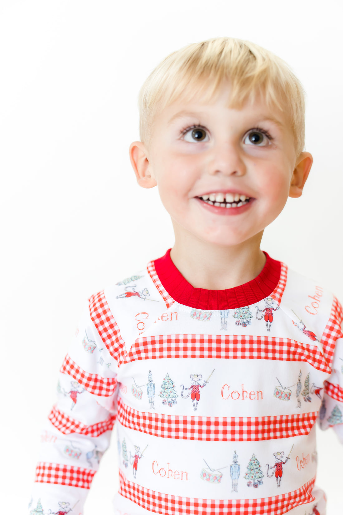 Little boy wearing personalized Modern Nutcracker Ballet for little boys with minimalistic images from the Nutcracker Ballet and his name with red checkered stripe pattern on white background and red cuffs.