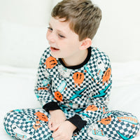 little boy wearing personalized halloween PJ's that have ghosts and skateboards and jack-o-lanterns on a black and white checkered background and black cuffs.