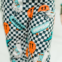 little boy wearing personalized halloween PJ's that have ghosts and skateboards and jack-o-lanterns on a black and white checkered background and black cuffs.