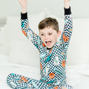 little boy wearing personalized halloween PJ's that have ghosts and skateboards and jack-o-lanterns on a black and white checkered background and black cuffs.