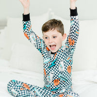 little boy wearing personalized halloween PJ's that have ghosts and skateboards and jack-o-lanterns on a black and white checkered background and black cuffs.