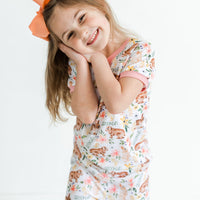 little girl wearing classic Easter bunny pajamas, Girl's custom aster pajamas with brown bunnies, and pink and yellow flowers scattered around white knit fabric along with her name, pale pink cuffs.
