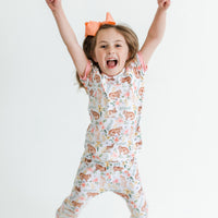 little girl wearing classic Easter bunny pajamas, Girl's custom aster pajamas with brown bunnies, and pink and yellow flowers scattered around white knit fabric along with her name, pale pink cuffs.
