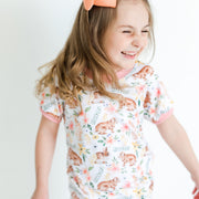 little girl wearing classic Easter bunny pajamas, Girl's custom aster pajamas with brown bunnies, and pink and yellow flowers scattered around white knit fabric along with her name, pale pink cuffs.