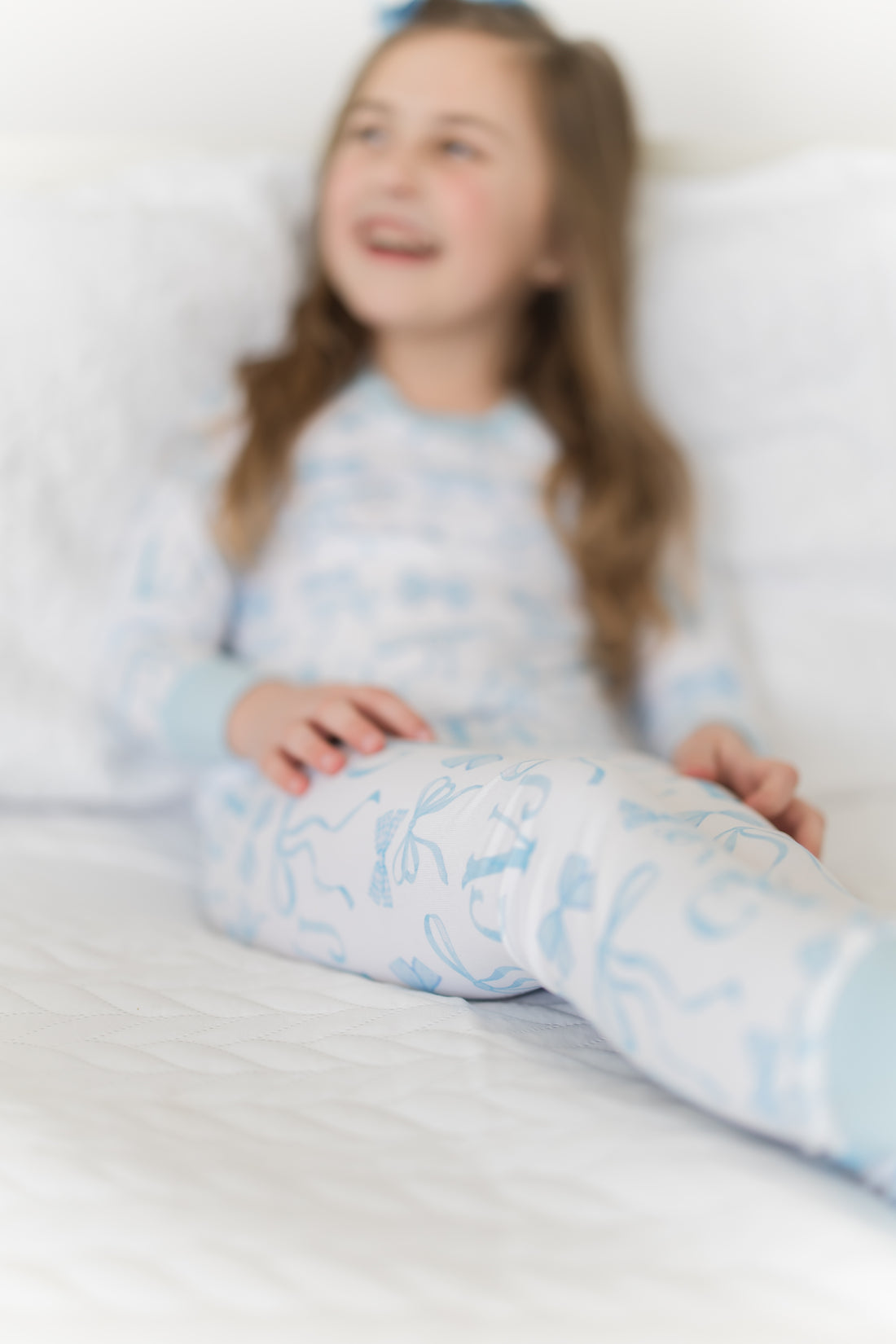 little girl wearing personalized little girl pjs with light blue bows and monogrammed initials on a white background and light blue cuffs.