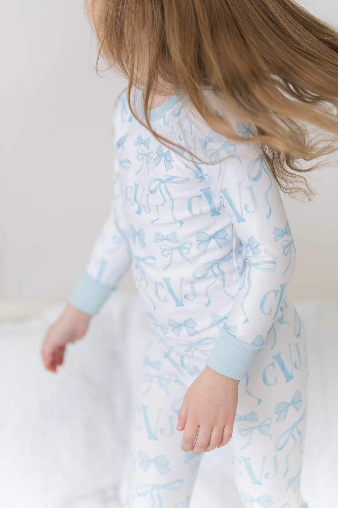 little girl wearing personalized little girl pjs with light blue bows and monogrammed initials on a white background and light blue cuffs.