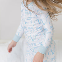 little girl wearing personalized little girl pjs with light blue bows and monogrammed initials on a white background and light blue cuffs.