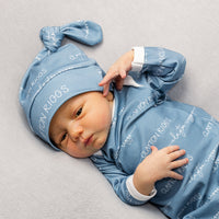 A newborn baby wearing a blue onesie with the word "CLAYTON RIGGS" printed on it, lying on a gray surface.