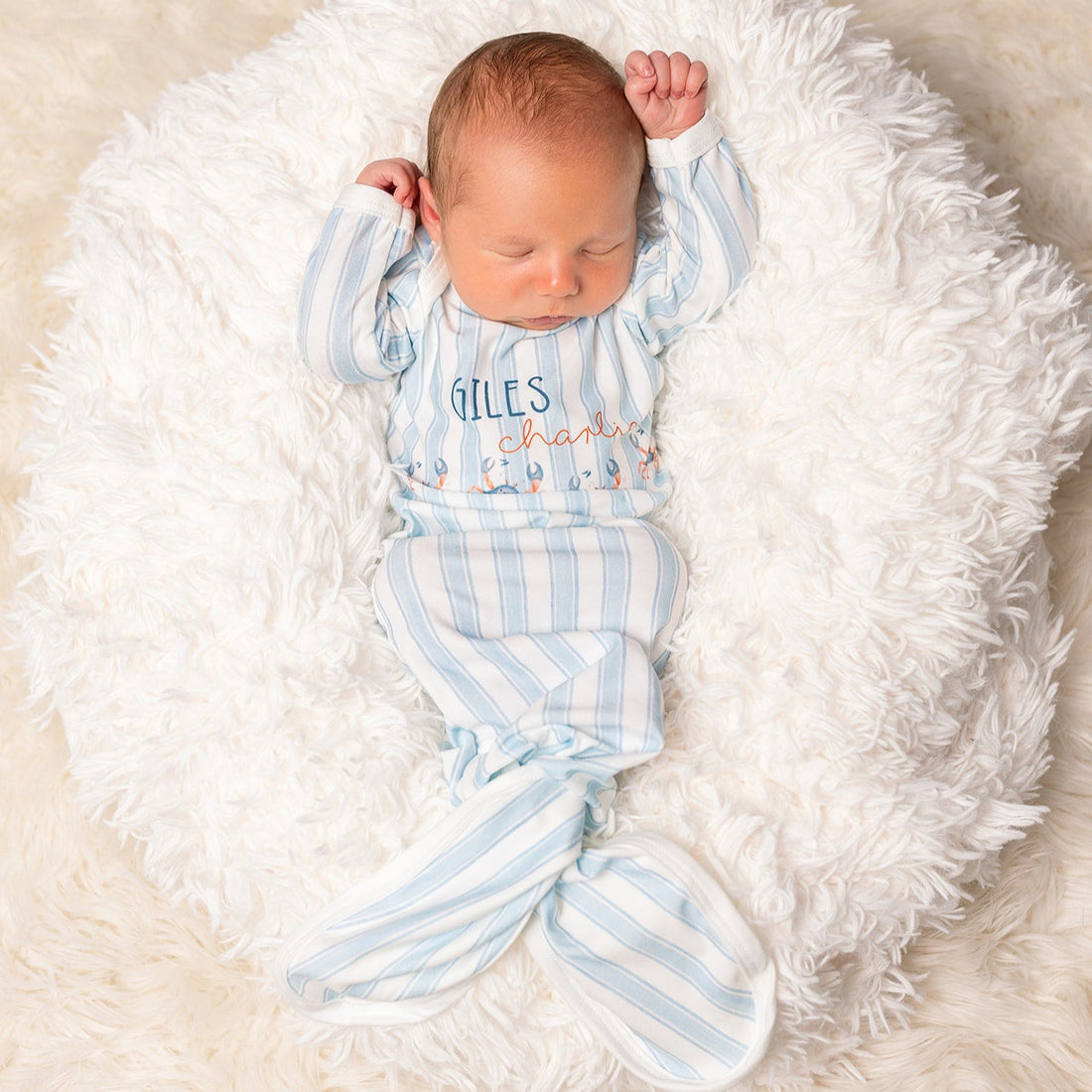 baby in a coastal inspired blue striped baby gown with little crabs, baby's name and tie bottle closure