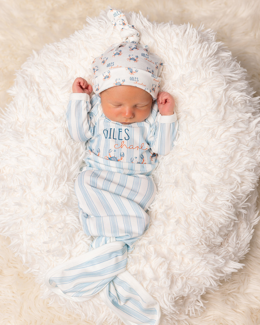 baby in a coastal inspired blue striped baby gown with little crabs, baby's name and tie bottle closure
