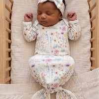 A newborn baby girl is peacefully sleeping in a wooden crib, wearing a white onesie with a floral print and a matching headband.
