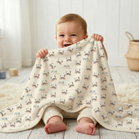 A smiling baby boy sitting on the floor, holding a blanket with a crab pattern.