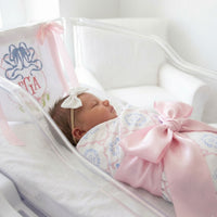 A newborn baby girl is peacefully sleeping in a hospital bed, wearing a pink bow and a white headband.