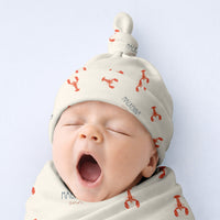 A sleeping baby wearing a white hat with red lobster designs.