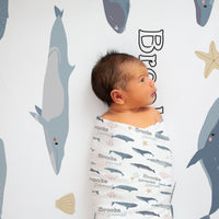 A baby is lying in a crib, wrapped in a blanket with a whale and starfish design.