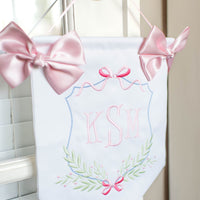 white and pink door hanging banner with baby's embroidered initials, two pink bows and a string for hanging on nursery or hospital door.