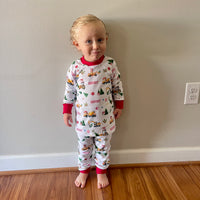 Baby standing in living room smiling while wearing Construction Christmas Pajamas.