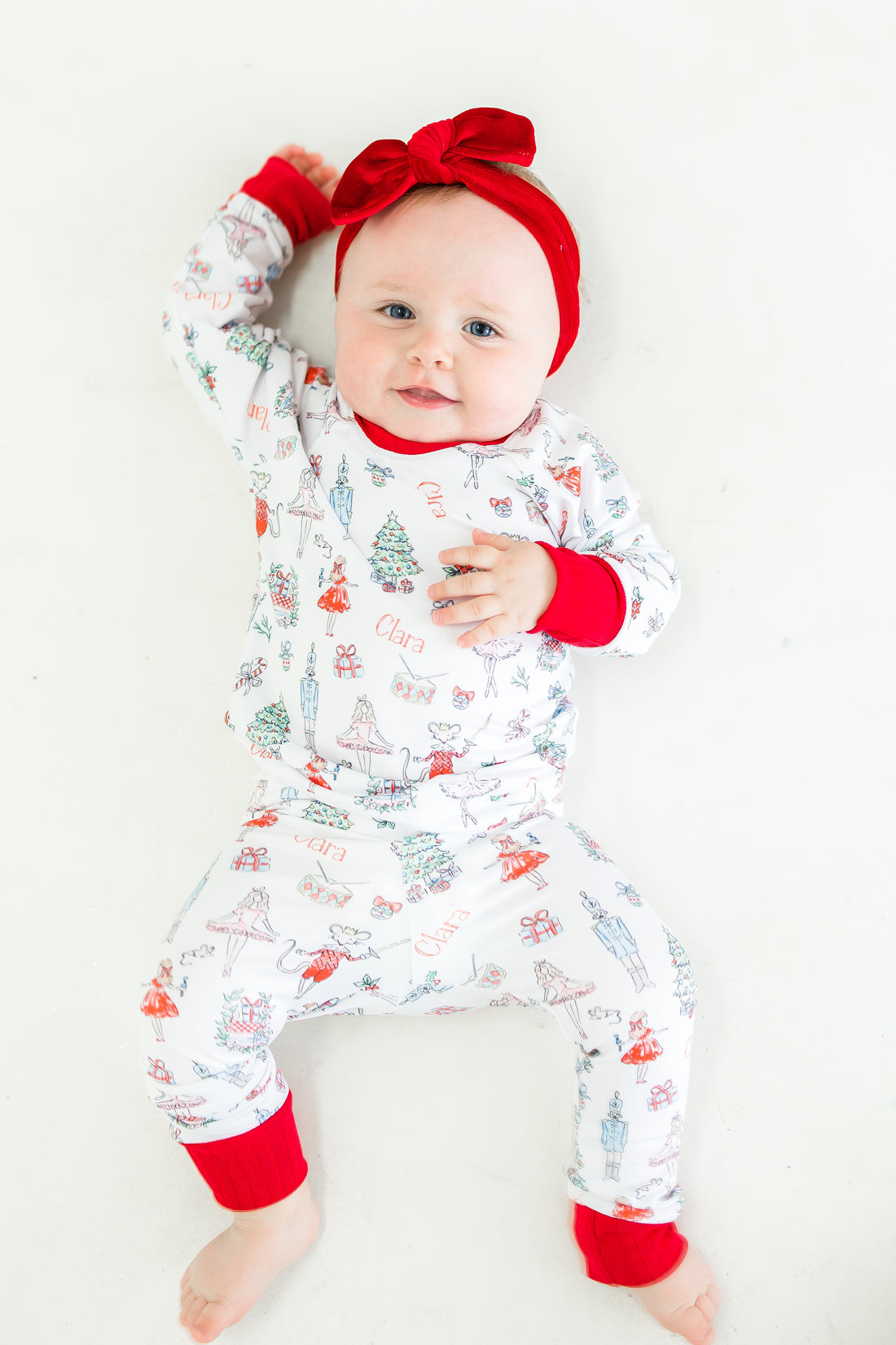 baby wearing personalized Nutcracker Ballet pajamas, featuring minimalistic images from the iconic nutcracker ballet among child's name on white fabric with red cuffs.
