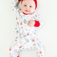 baby wearing personalized Nutcracker Ballet pajamas, featuring minimalistic images from the iconic nutcracker ballet among child's name on white fabric with red cuffs.