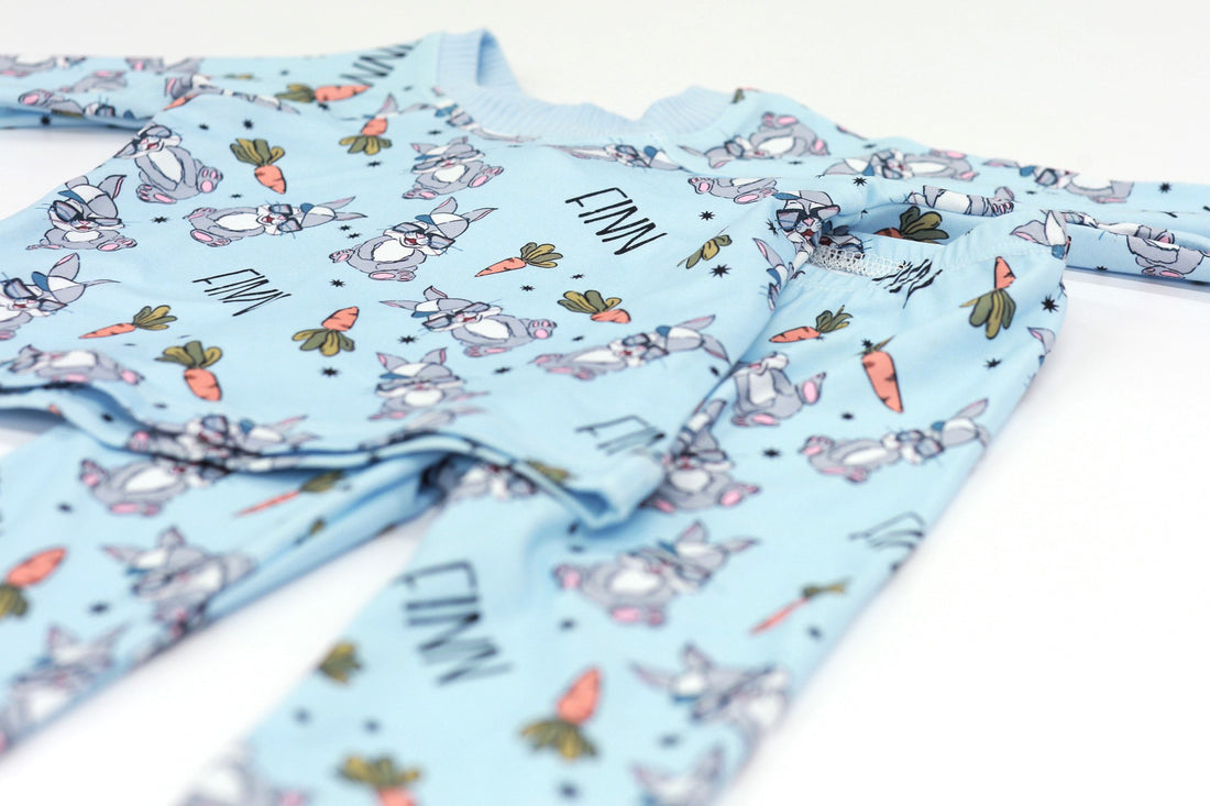 boys easter personalized pajamas featuring his name, hip easter bunnies in glasses and hats, and cartoon carrots on light blue stretchy knit fabric.