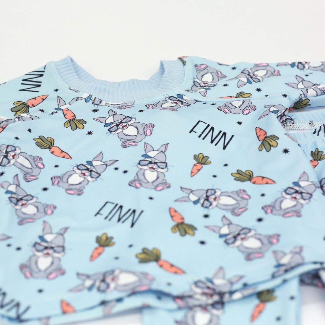 boys easter personalized pajamas featuring his name, hip easter bunnies in glasses and hats, and cartoon carrots on light blue stretchy knit fabric.