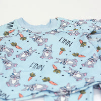 boys easter personalized pajamas featuring his name, hip easter bunnies in glasses and hats, and cartoon carrots on light blue stretchy knit fabric.
