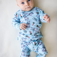 baby boy wearing boys easter personalized pajamas featuring his name, hip easter bunnies in glasses and hats, and cartoon carrots on light blue stretchy knit fabric.
