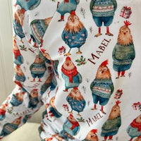 Little girl wearing personalized festive chickens christmas pajamas that feature cute chickens wearing sweaters and scarves on a white background and red cuffs.