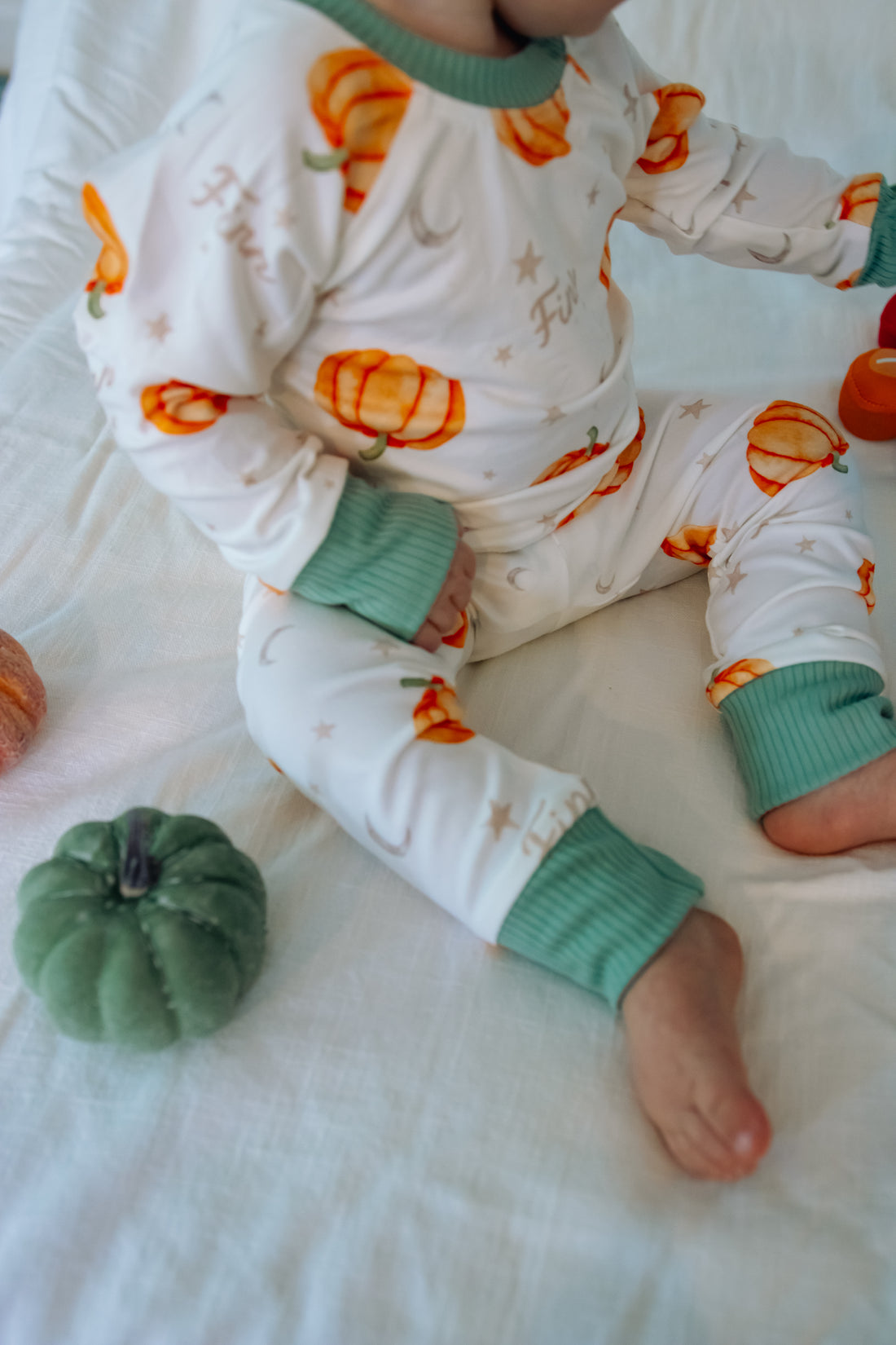 Baby wearing Autumn PJ's with orange pumpkins and baby's name on white background with green cuffs
