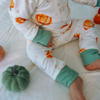 Baby wearing Autumn PJ's with orange pumpkins and baby's name on white background with green cuffs