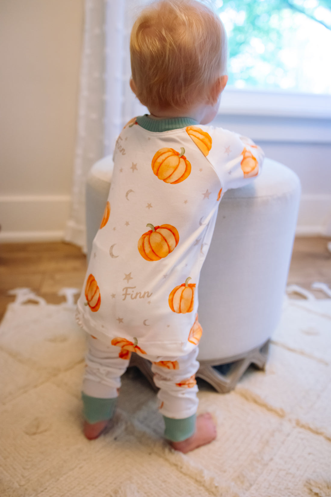 Baby wearing Autumn PJ's with orange pumpkins and baby's name on white background with green cuffs