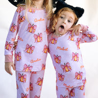 Two young girls wearing matching Halloween nightwear for kids with cartoon pumpkins and pink bows