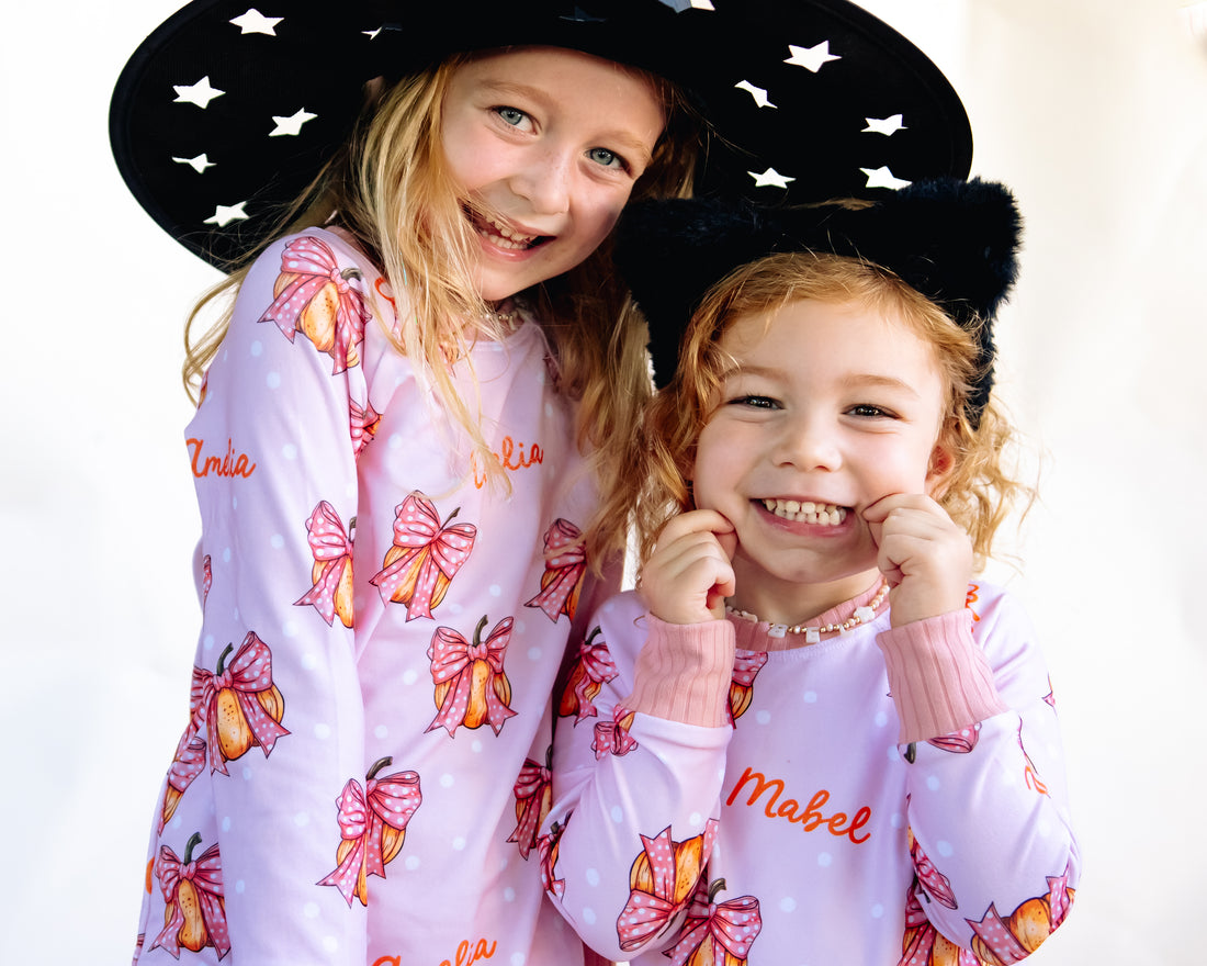 Two young girls wearing matching Halloween nightwear for kids with cartoon pumpkins and pink bows