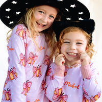Two young girls wearing matching Halloween nightwear for kids with cartoon pumpkins and pink bows