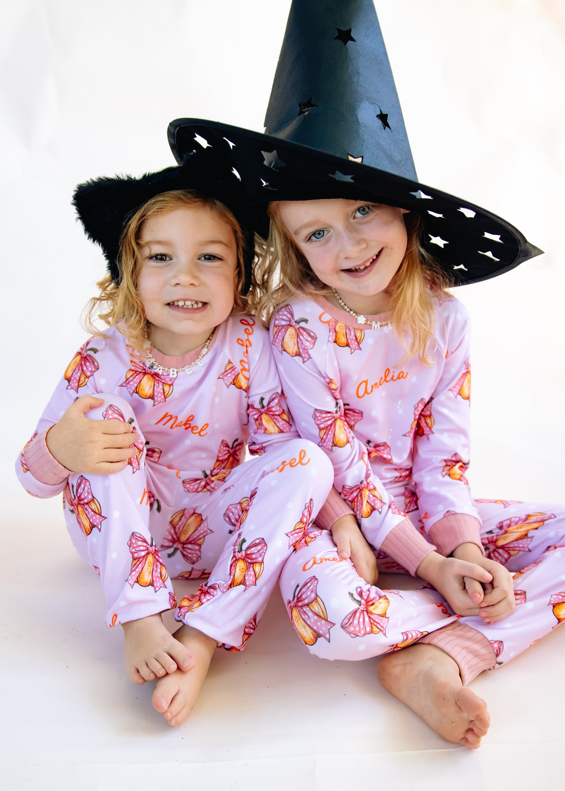 Two young girls wearing matching Halloween nightwear for kids with cartoon pumpkins and pink bows